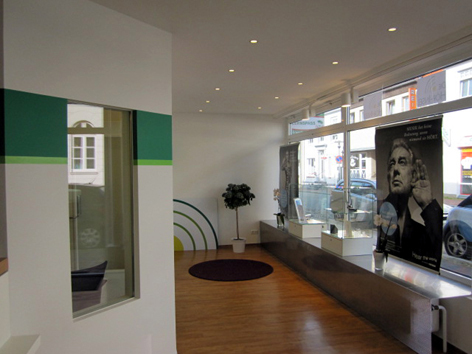 Modernes Ladenlokal mit großen Fenstern, Holzfußboden und Werbeplakaten im Schaufenster.